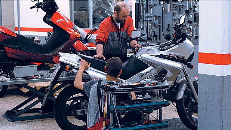Autogarage Foto van een werkplaats waar twee mensen aan een motorfiets werken.